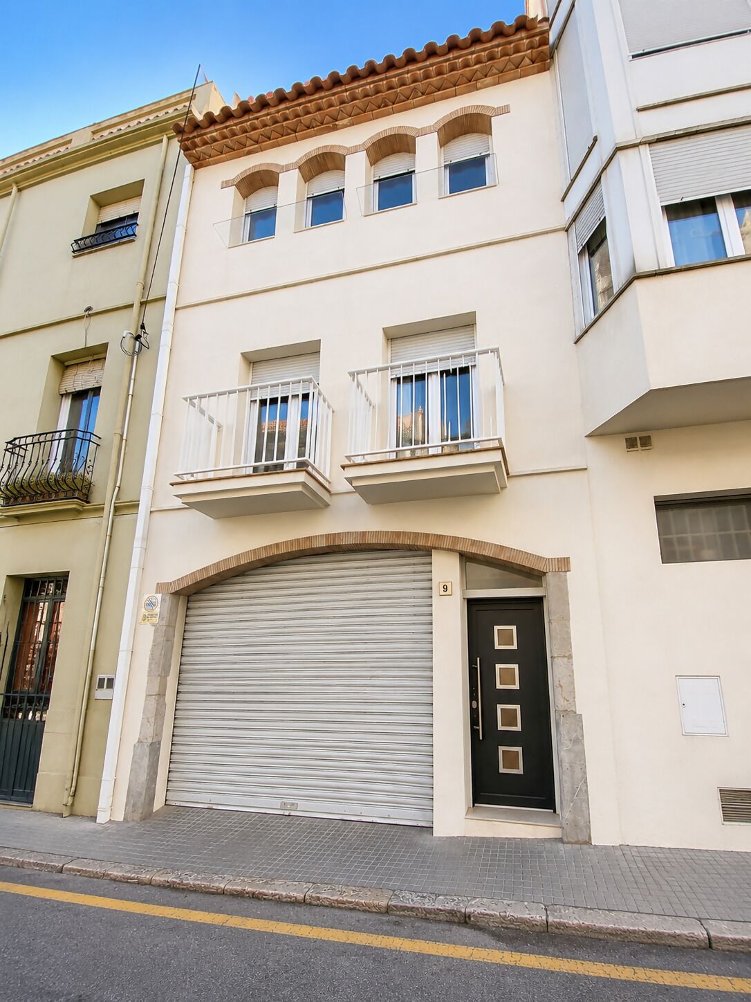 Un edificio de varios pisos con puerta de garaje, balcones y cielo despejado.