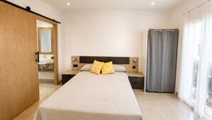 A bedroom with a bed, bedside tables, a mirror, a wardrobe, and a window with curtains. - Apartaments l'Escala Centre  3 (Escala, L')