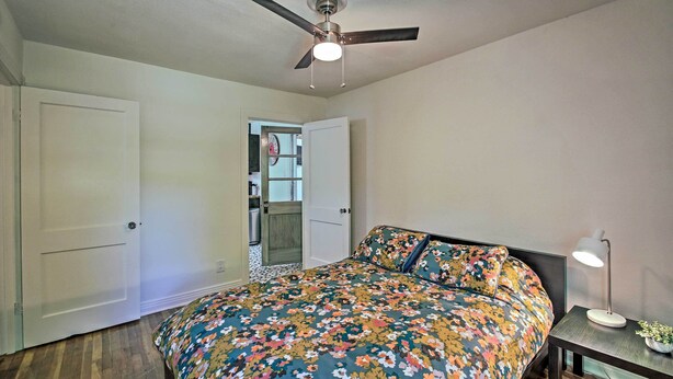 A bedroom with a bed, a ceiling fan, a nightstand with a lamp, and a door leading to another room. - Walk to Oaklawn Racing: Hot Springs Home! (Hot Springs)