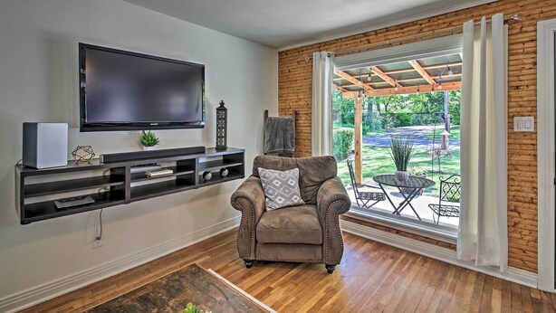 Una sala de estar con televisor de pantalla plana, un sillón de cuero marrón, piso de madera y vistas a un patio con mobiliario exterior.