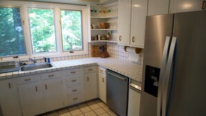 Eine moderne Küche mit weißen Schränken, einem Edelstahlkühlschrank und einem Fenster mit Blick auf Bäume.