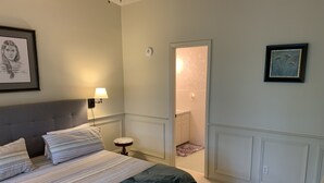 Ein Schlafzimmer mit einem Bett, einem Nachttisch, einer Lampe, einem gerahmten Bild und einer Tür zu einem Badezimmer.