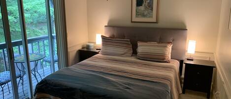 Un dormitorio con una cama grande, dos mesitas de noche con lámparas, un cuadro sobre la cama y un balcón con sillas.