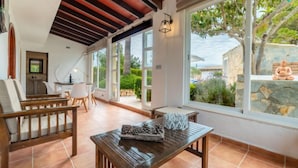 Eine geräumige Terrasse mit einem Holztisch und -stühlen, große Fenster mit Blick auf den Garten und eine Steinmauer.