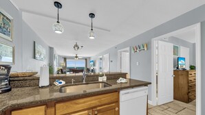 A modern kitchen with granite countertops, wooden cabinets, and a built-in dishwasher. There are pendant lights, a large window, and a view of the ocean. - Beach front condo; great location; with pool  (Orange Beach)