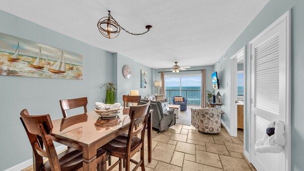 A dining area with a wooden table and chairs, a ceiling fan, and a painting of sailboats on the wall. - Beach front condo; great location; with pool  (Orange Beach)