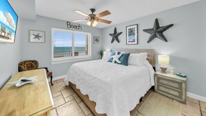 A bedroom with a bed, a desk, a ceiling fan, starfish decorations, and a window with a view of the beach. - Beach front condo; great location; with pool  (Orange Beach)