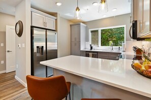 A modern kitchen with stainless steel appliances, a large island, and a view of greenery outside. - Fun South Slope Townhome (Asheville)