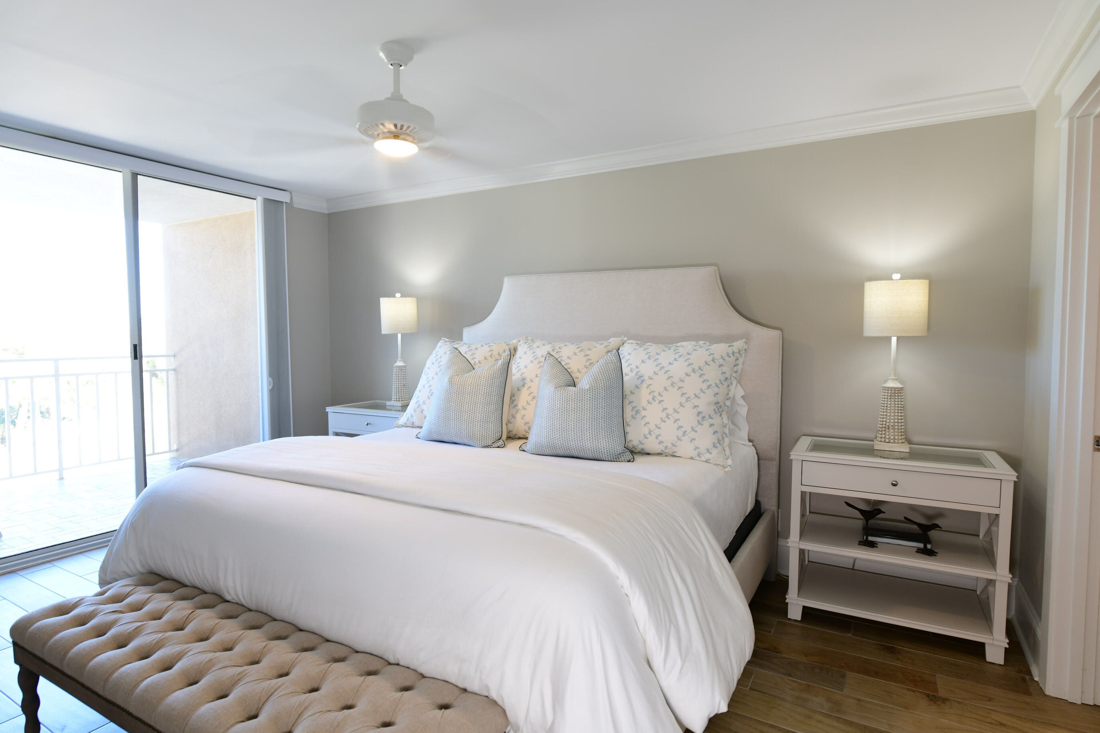 A bedroom with a large bed, two bedside tables with lamps, a bench, and a view of the outdoors.