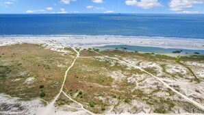 Une vue aérienne d’une zone côtière avec une plage, un ciel dégagé et un navire au loin.
