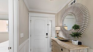 Un couloir avec une porte blanche, un miroir décoratif, une commode en bois et une petite plante en pot.