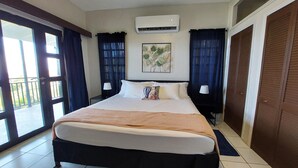 A hotel room with a large bed, an air conditioner, a window with curtains, and a door. - PASSION FRUIT Apartment for work or getaway (St. Thomas)