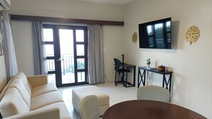 A living room with a sofa, a dining table, and a TV mounted on the wall. - PASSION FRUIT Apartment for work or getaway (St. Thomas)