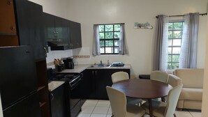 A compact kitchen with dark cabinets, a stove, and a dining area with a table and chairs. - PASSION FRUIT Apartment for work or getaway (St. Thomas)