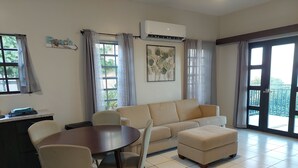A living room with a sofa, ottoman, dining table, chairs, and a kitchen area with a counter and sink. - PASSION FRUIT Apartment for work or getaway (St. Thomas)