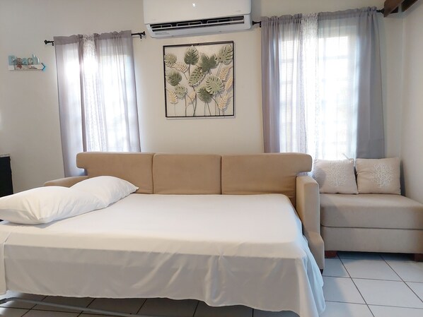 A bedroom with a bed, a sofa, and a wall-mounted air conditioner. - PASSION FRUIT Apartment for work or getaway (St. Thomas)