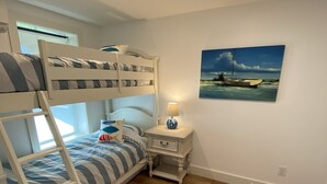 Una camera con letti a castello, pavimento in legno, un comodino con lampada e un quadro raffigurante una barca al muro.