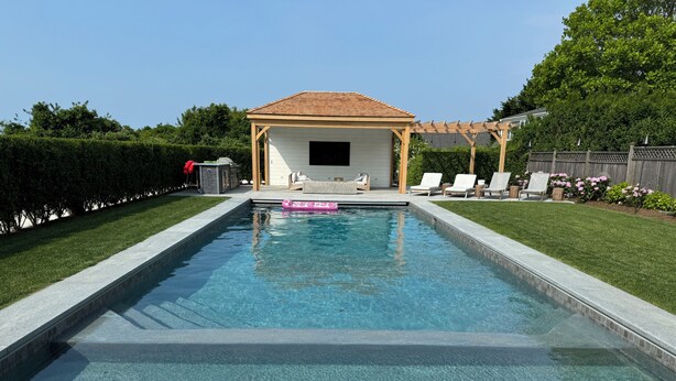 Una piscina rettangolare con acqua cristallina, circondata da un prato curato e un pergolato in legno.
