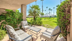 Eine überdachte Terrasse mit Gartenmöbeln, Blick auf einen Golfplatz und hohe Palmen.