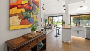 Eine moderne Küche mit einer großen Kochinsel, einem Essbereich inklusive Sofa und Couchtisch sowie einem farbenfrohen, abstrakten Gemälde an der Wand.