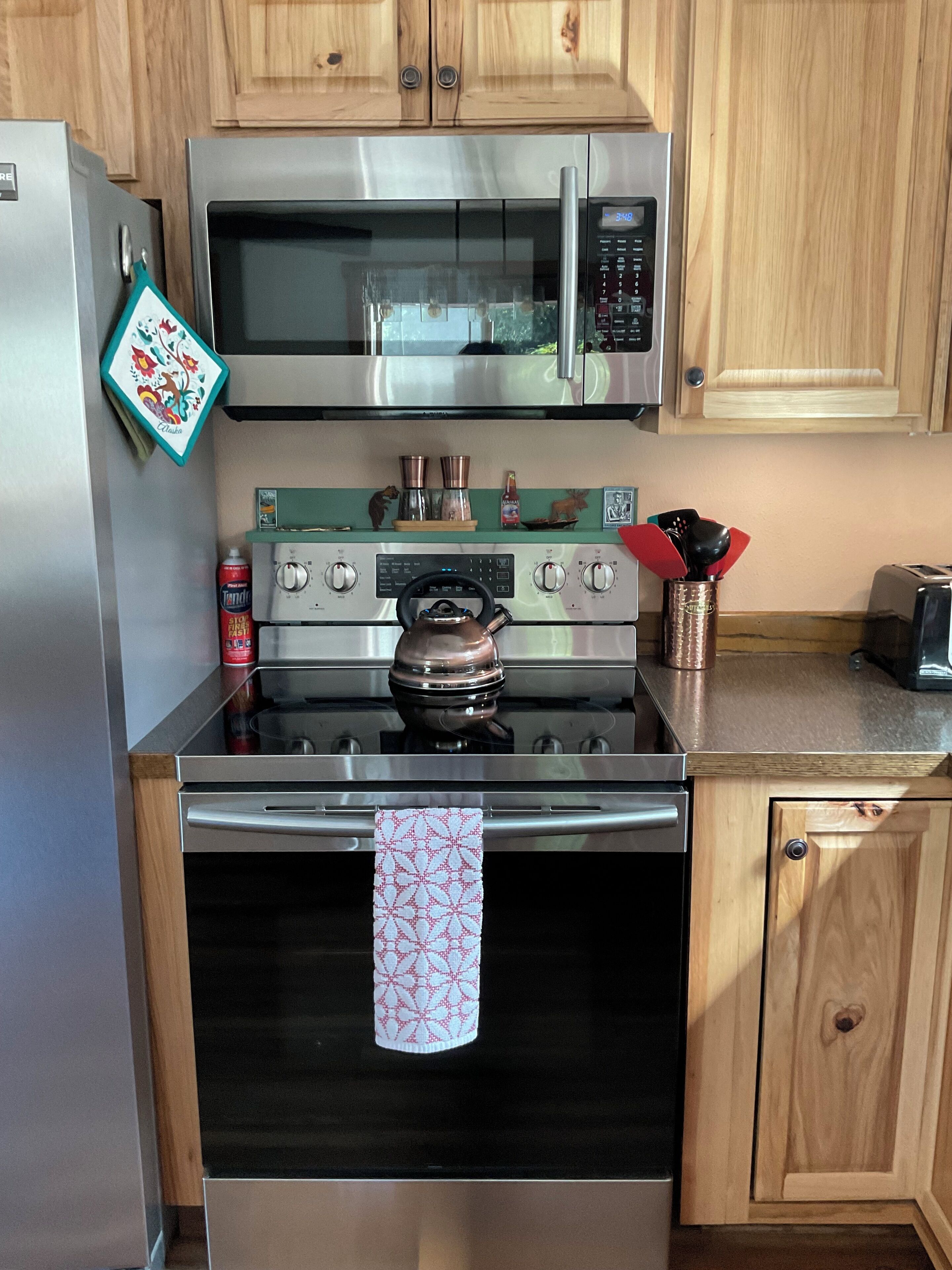 A kitchen with a stainless steel refrigerator, a microwave, a stove, and wooden cabinets.