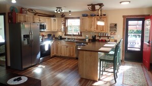 A kitchen with wooden cabinets, a stainless steel refrigerator, a microwave, and a sink. There is a dining area with a table and chairs. - Resurrection Peaks Lodge.  Upper unit sleeps 6, private lot and close to town. (Seward)