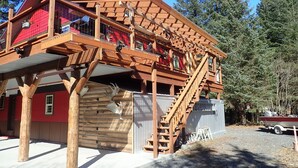 A wooden cabin with a red exterior, a balcony, and a staircase leading to an upper level. - Resurrection Peaks Lodge.  Upper unit sleeps 6, private lot and close to town. (Seward)