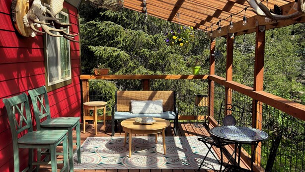 A wooden deck with a red wall, a bench, and a table with chairs. - Resurrection Peaks Lodge.  Upper unit sleeps 6, private lot and close to town. (Seward)
