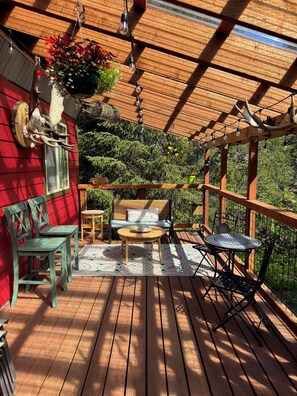 A wooden deck with a red wall, a bench, and a table with chairs. - Resurrection Peaks Lodge.  Upper unit sleeps 6, private lot and close to town. (Seward)