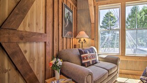 Una habitación acogedora con paredes de madera, un sofá con cojines estampados, una lámpara y una ventana con vistas a árboles.