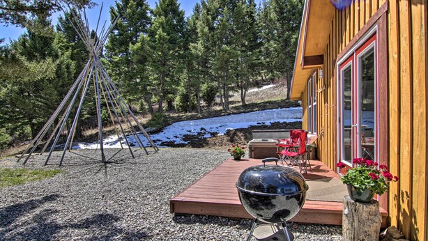 Una cabaña de madera con un porche, una tienda tipi y una parrilla.