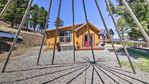 Una cabaña de madera con puerta roja, un patio con muebles exteriores y un camino de entrada de grava.
