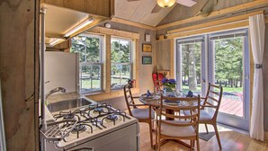 Una cocina con estufa a gas, pileta y muebles bajos de madera. Hay ventanas amplias y un ventilador de techo.