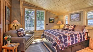 Una habitación cálida tipo cabaña con una cama, un sofá y una ventana con vistas a un bosque.