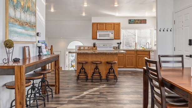 A modern kitchen with wooden cabinets, a central island with stools, and a dining table. - Cozy House Near Boise State University, Downtown and Boise River Greenbelt. (Boise)