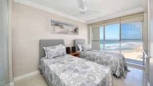 A bedroom with two beds, a ceiling fan, a beach view, and a framed picture on the wall.