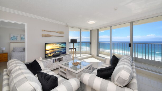 A modern living room with a large window overlooking the ocean, a flat-screen TV, and a cozy seating area.