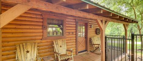 A wooden cabin with a porch, two rocking chairs, and a metal gate.