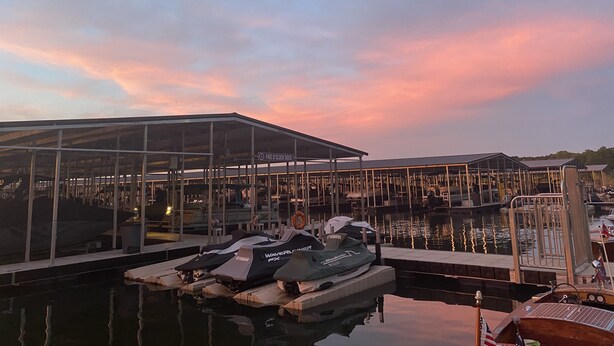 A marina with boats docked, a covered area labeled "FIVE O'CLOCK DOCK," and a sunset sky.