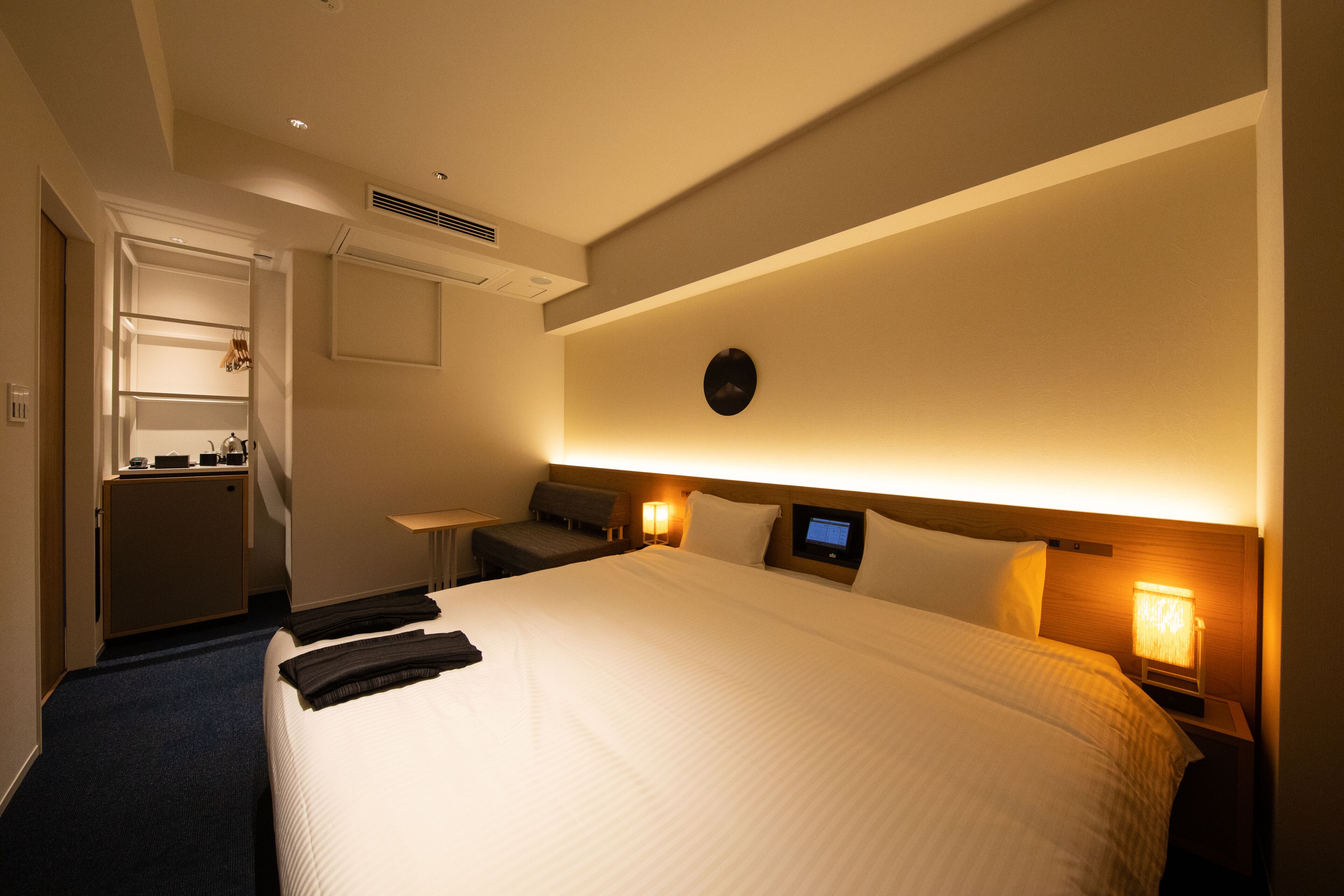 Una habitación de hotel con una cama grande, mesitas de noche con lámparas, un escritorio pequeño y un armario.