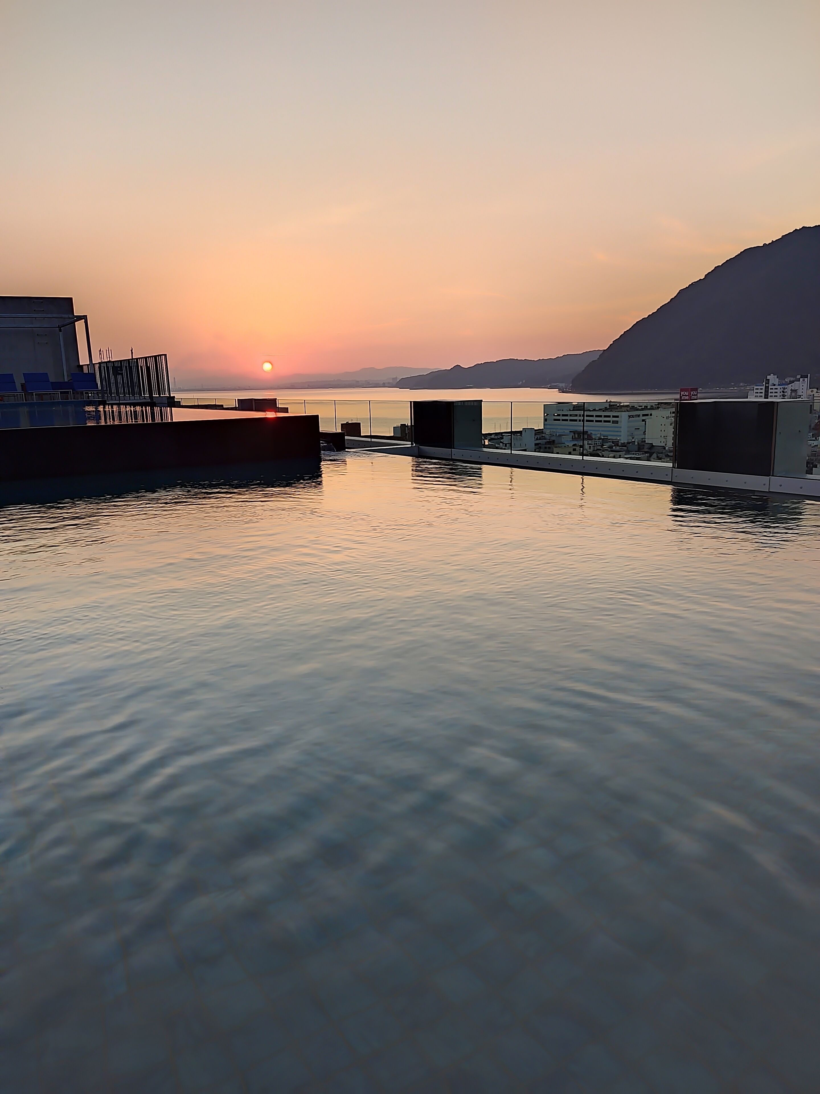 Vista al agua con un atardecer, agua tranquila y edificios al fondo.