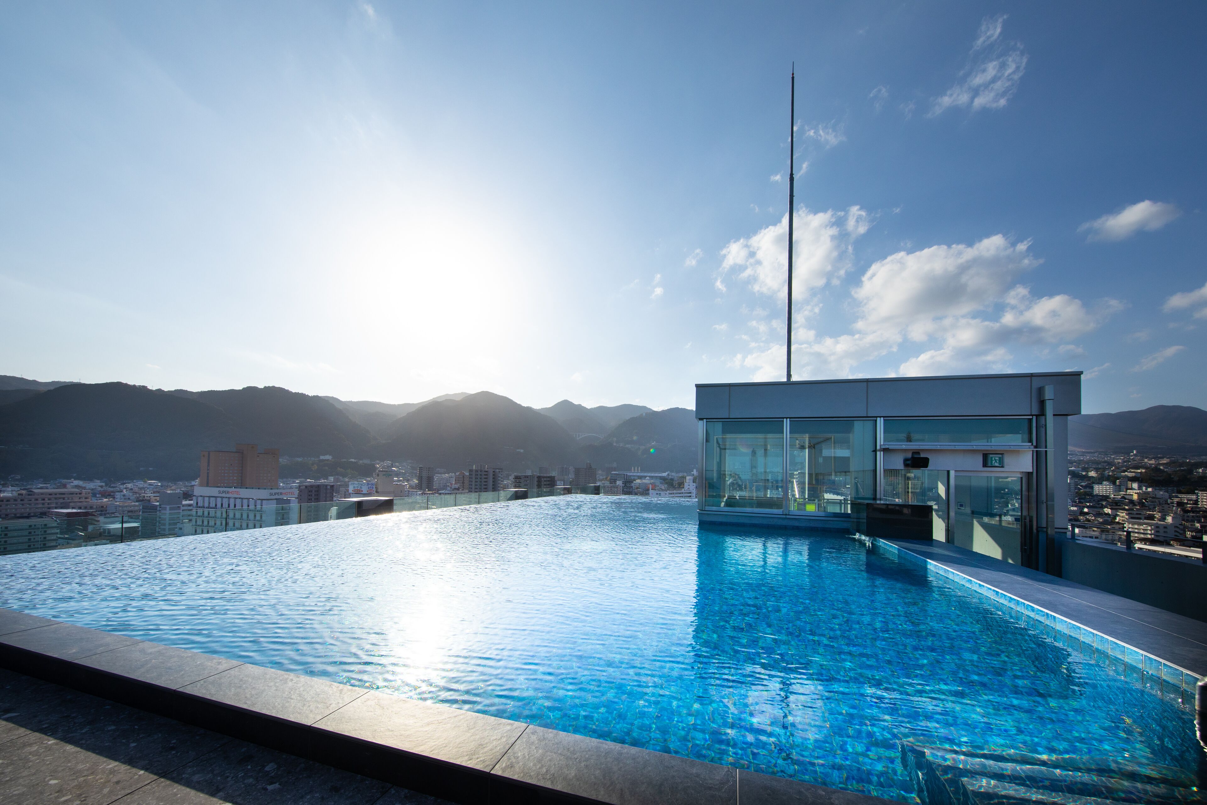 A rooftop infinity pool with a glass enclosure and a cityscape view in the background.