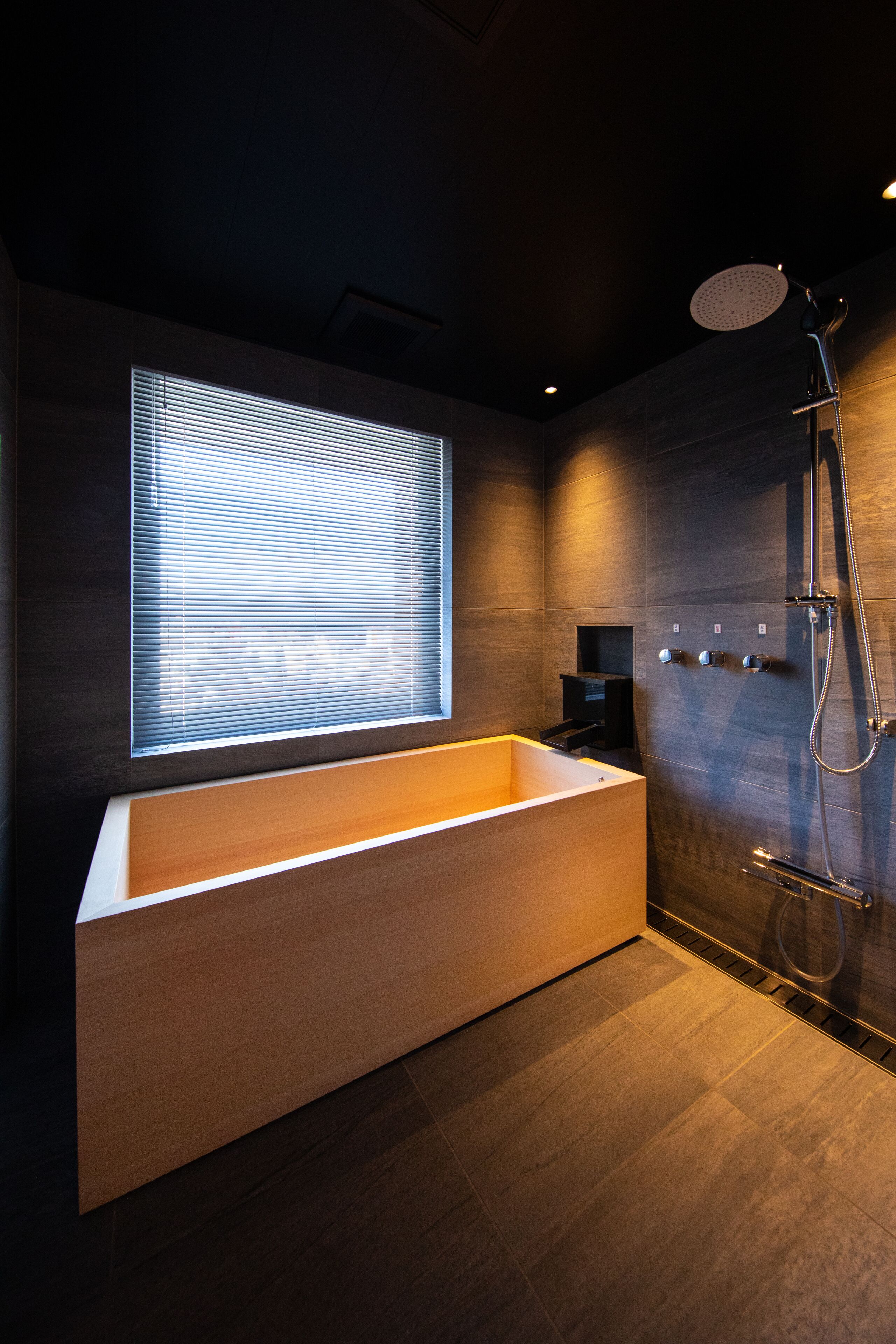 Een moderne badkamer met een groot bad, een douche en een raam met zonwering.
