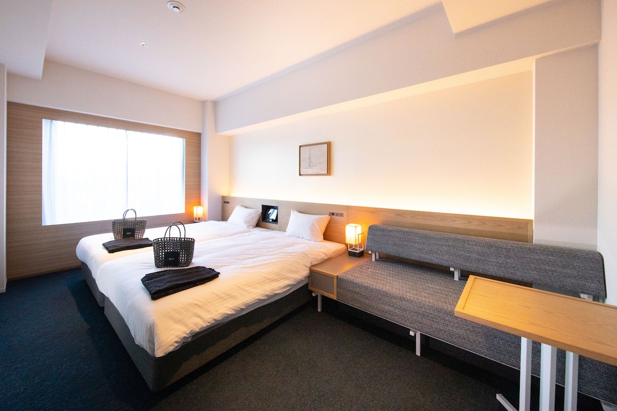 A hotel room with a large bed, a bench, a small table, and a window.