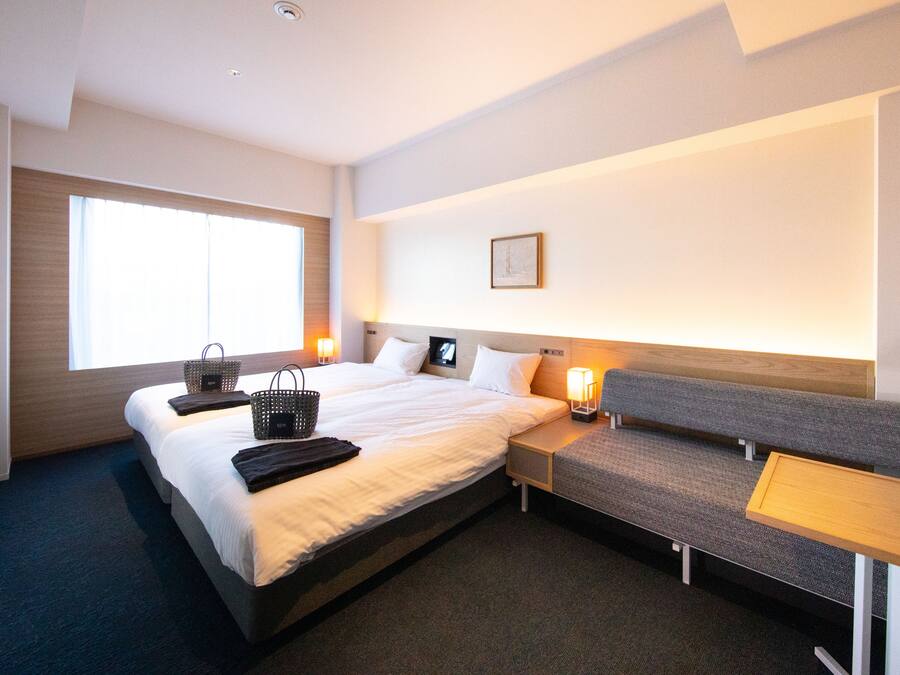 Ein Hotelzimmer mit einem großen Bett, einer Bank, einem kleinen Tisch und einem Fenster.