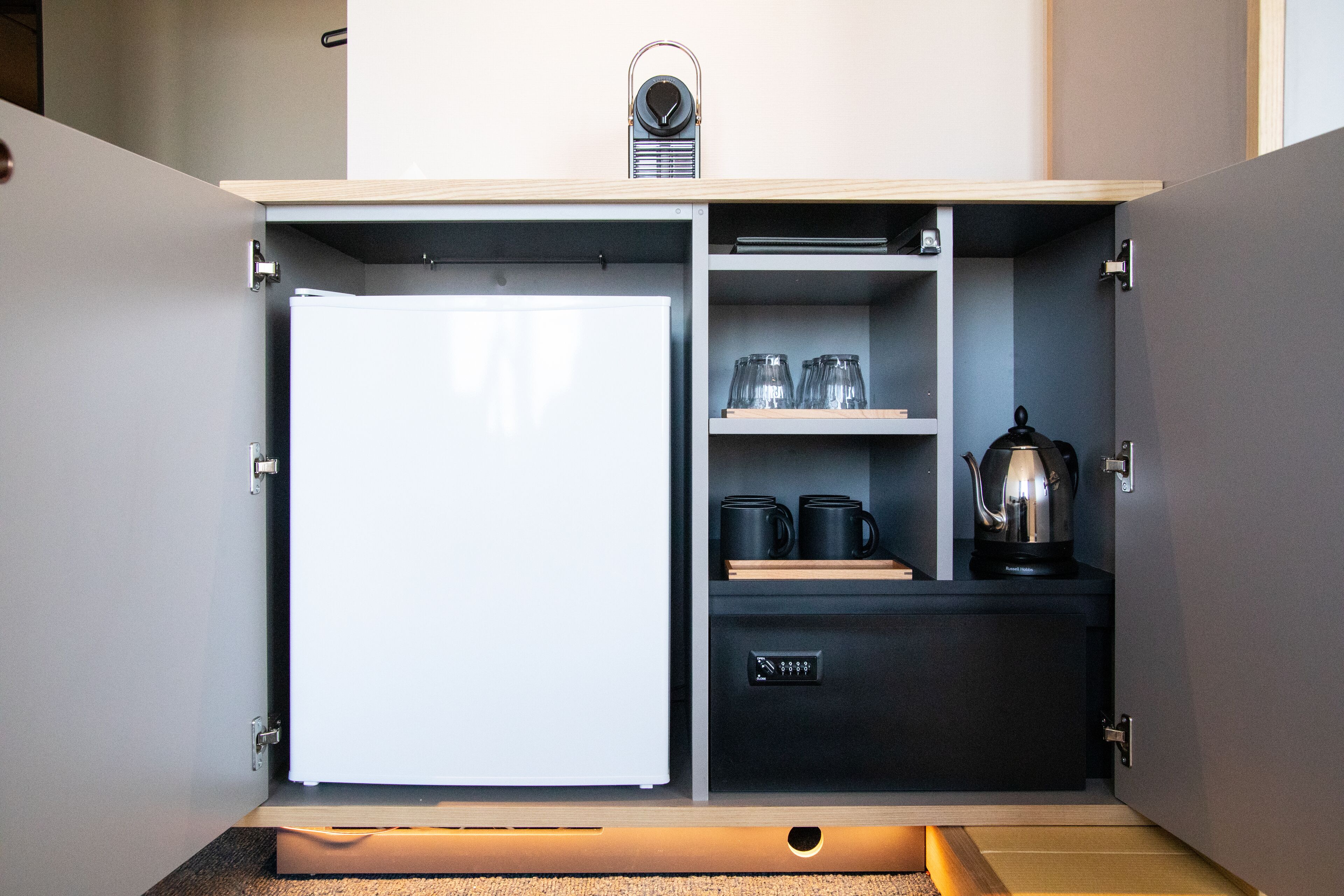 A compact kitchenette with a built-in refrigerator, a coffee maker, and a kettle.