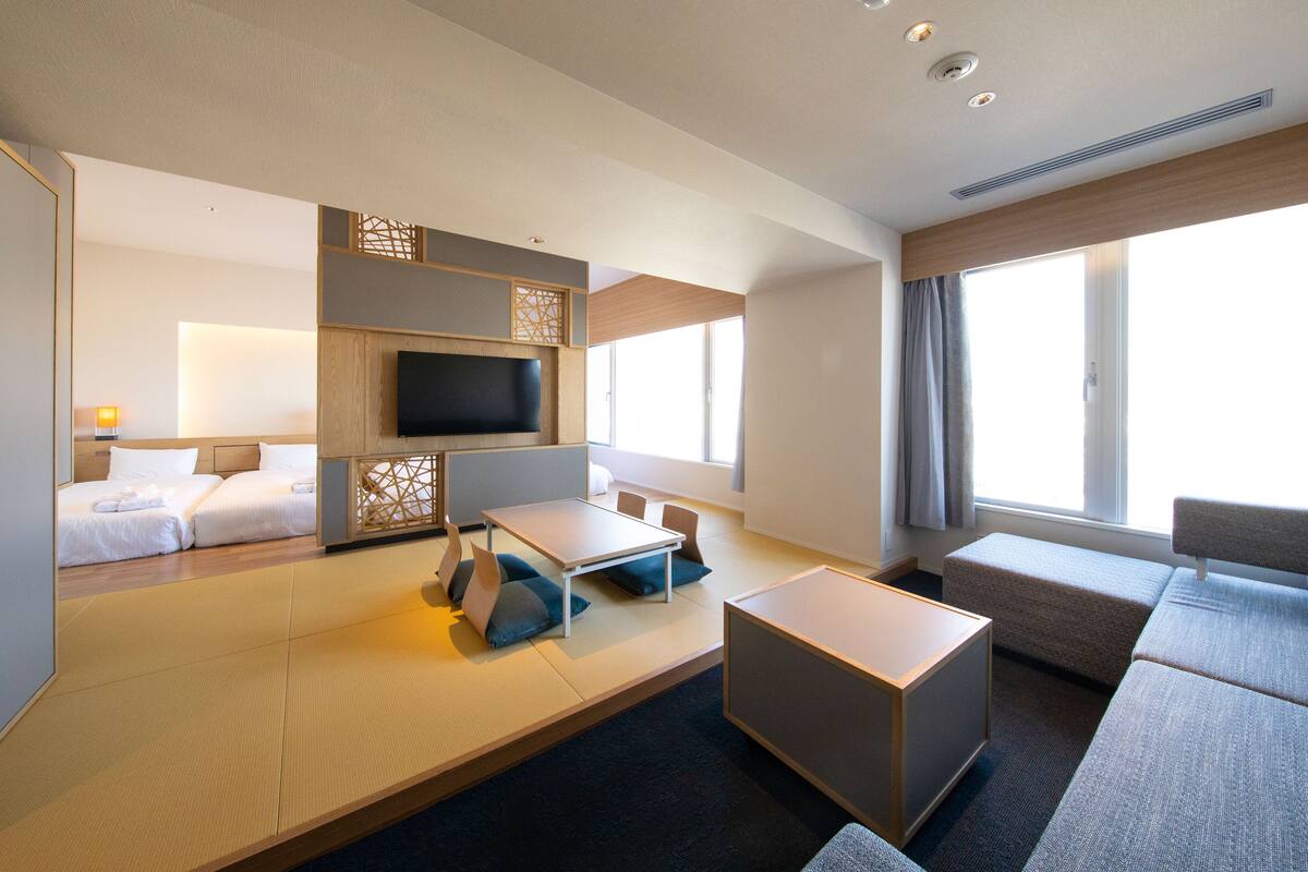 A modern hotel room with a sofa, a small table, a TV, and a bed.