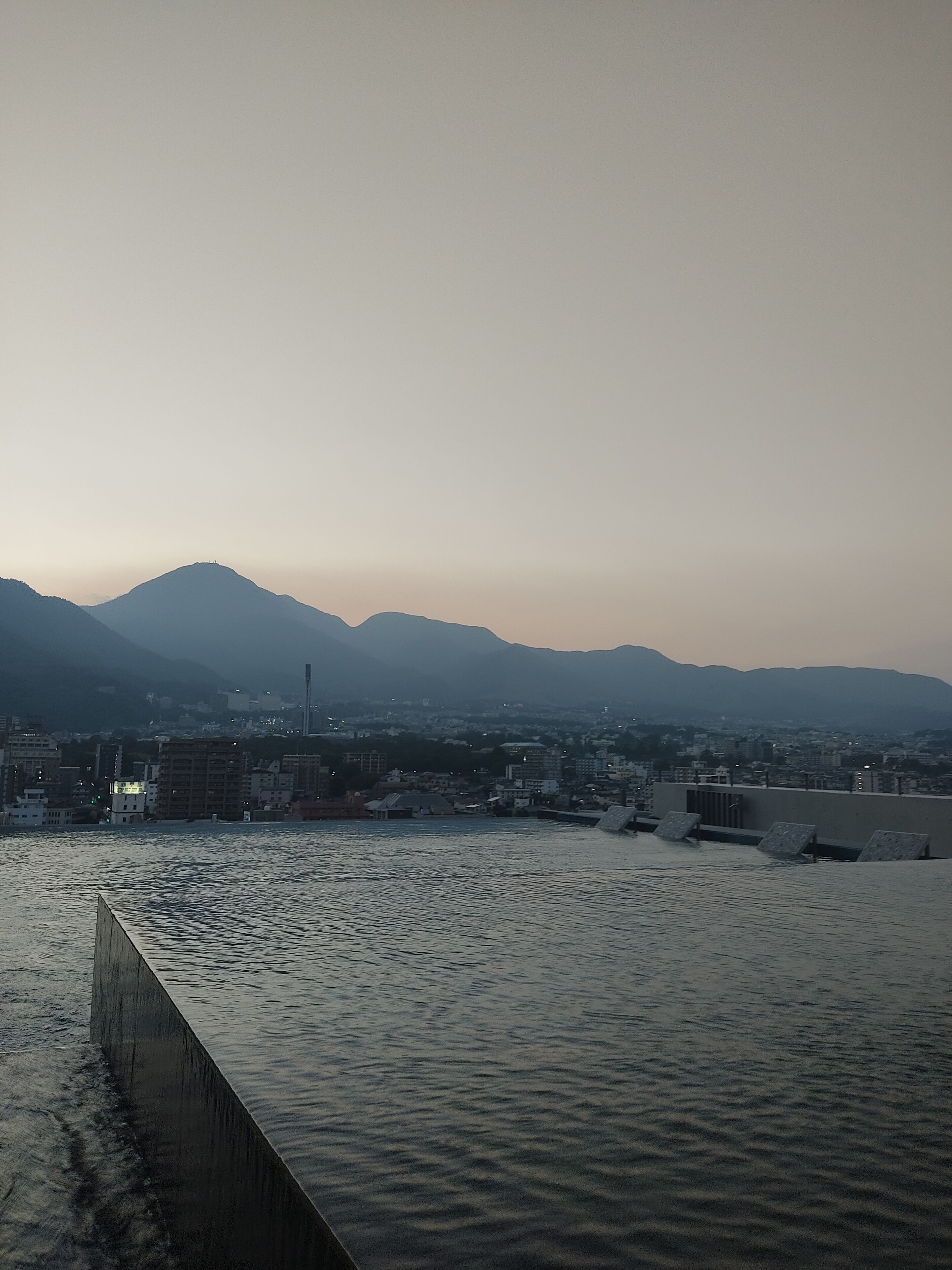 A waterfront view with a cityscape in the background, including mountains and buildings.