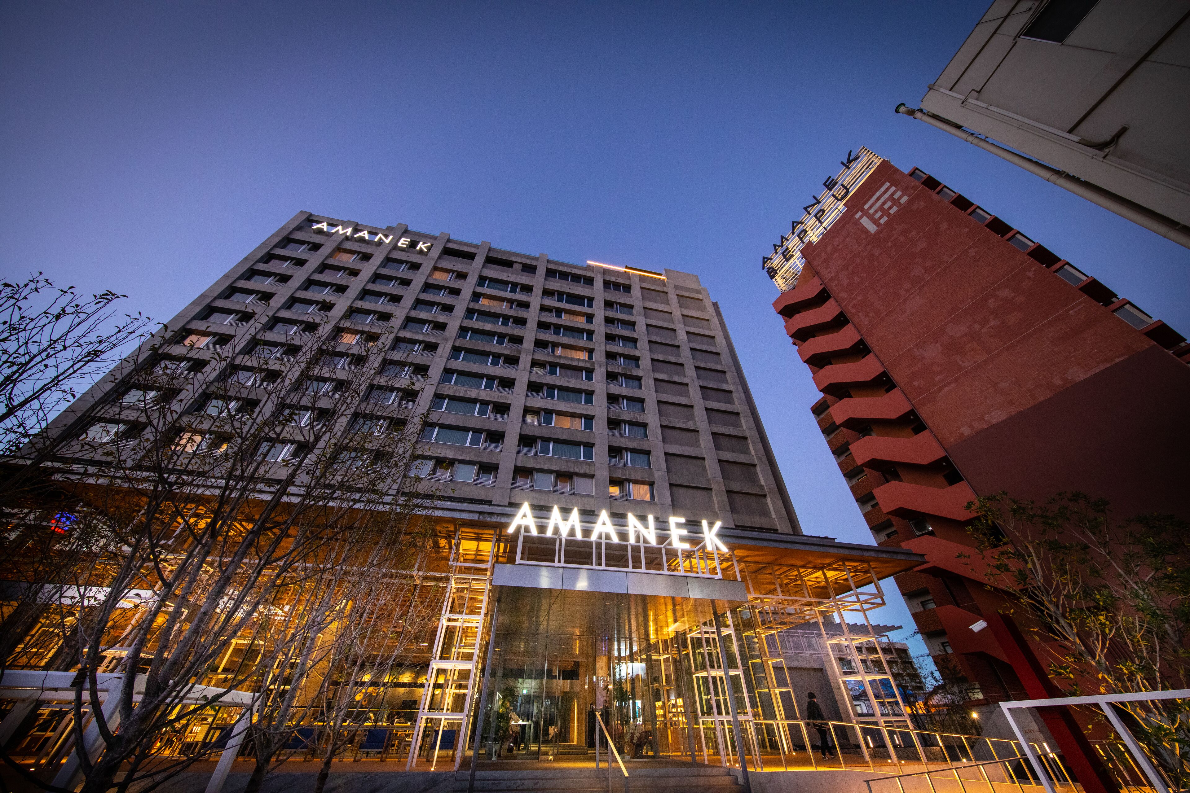 Un hôtel moderne, reconnaissable à son imposante enseigne « AMANEX », doté d’une façade en verre et d’une entrée à l’architecture soignée.