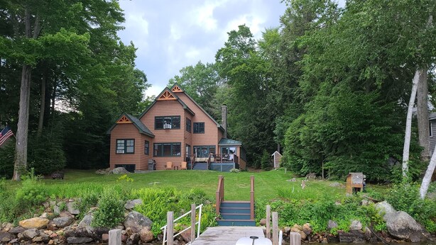 Eine Holzanlegestelle führt zu einem Haus mit Terrasse und einem kleinen Boot.